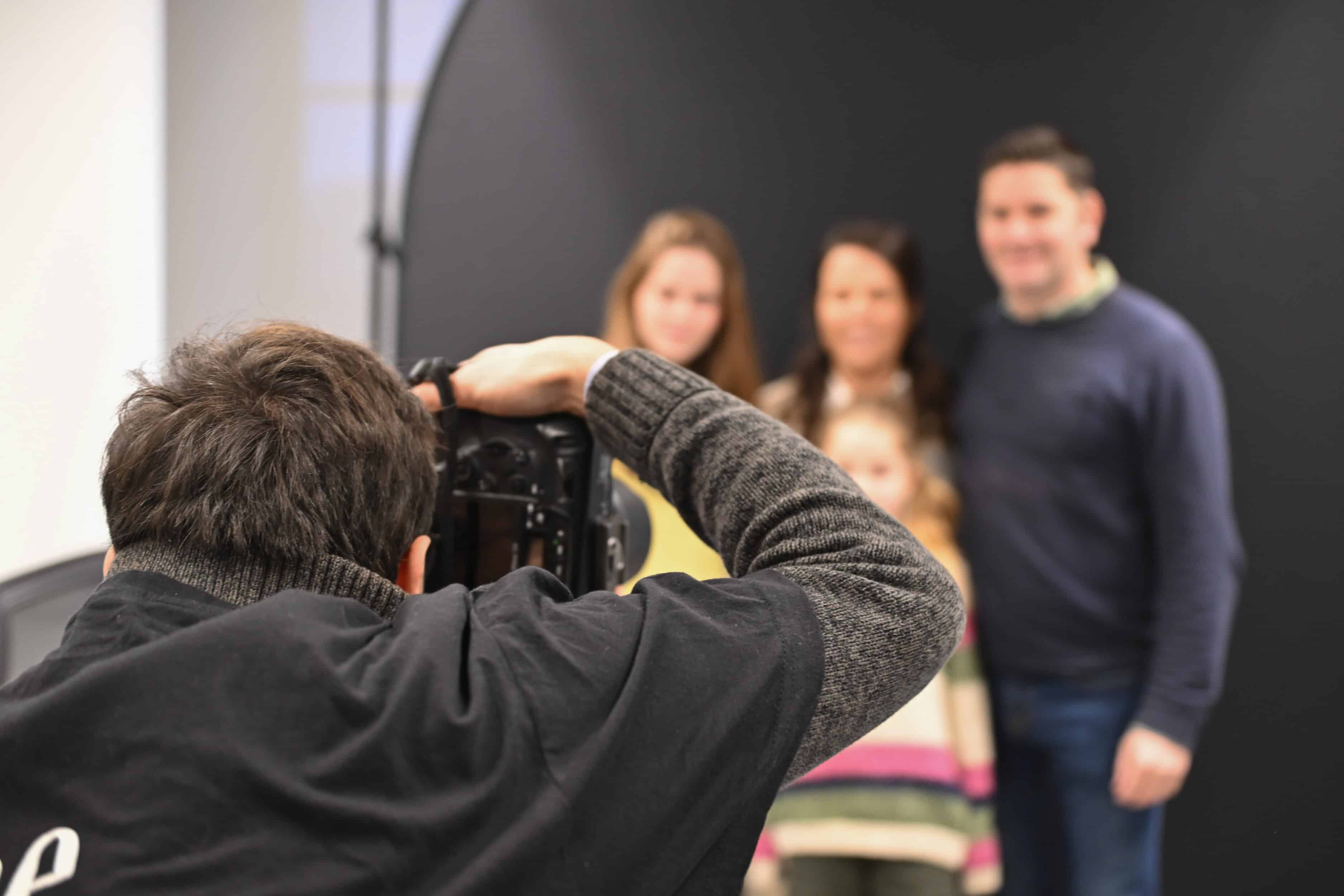 Un photographe capture un moment chaleureux lors d'une séance photo événementielle organisée par CheeeseBOX avec une famille souriante sur fond noir.
