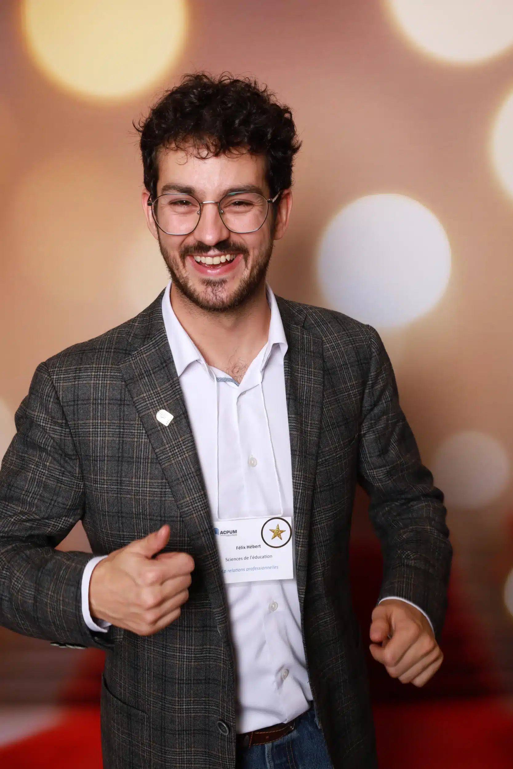 Un homme souriant pose dans un photobooth CheeeseBOX, vêtu d'un blazer à carreaux et portant un badge. Le fond flou crée une atmosphère festive.